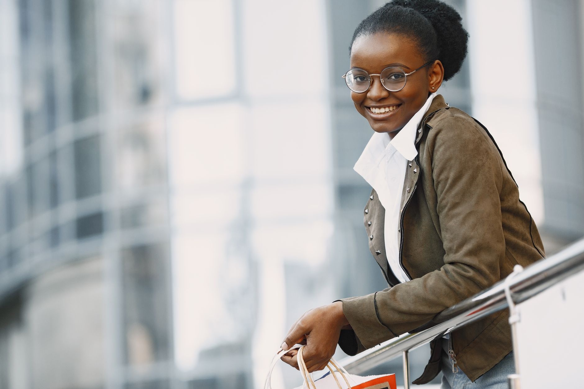 Smiling woman with eyeglasses holding a shopping bag outdoors.