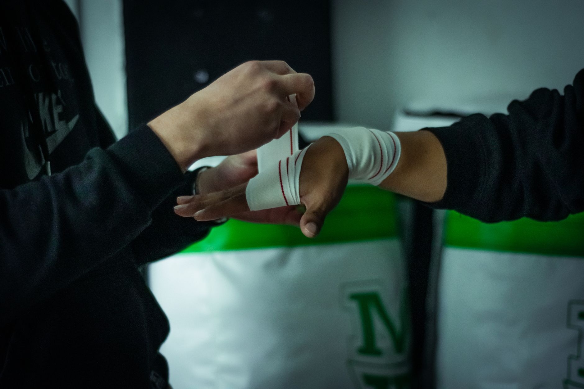 A close-up view of a trainer wrapping a boxer's hand with bandages in a gym setting.
