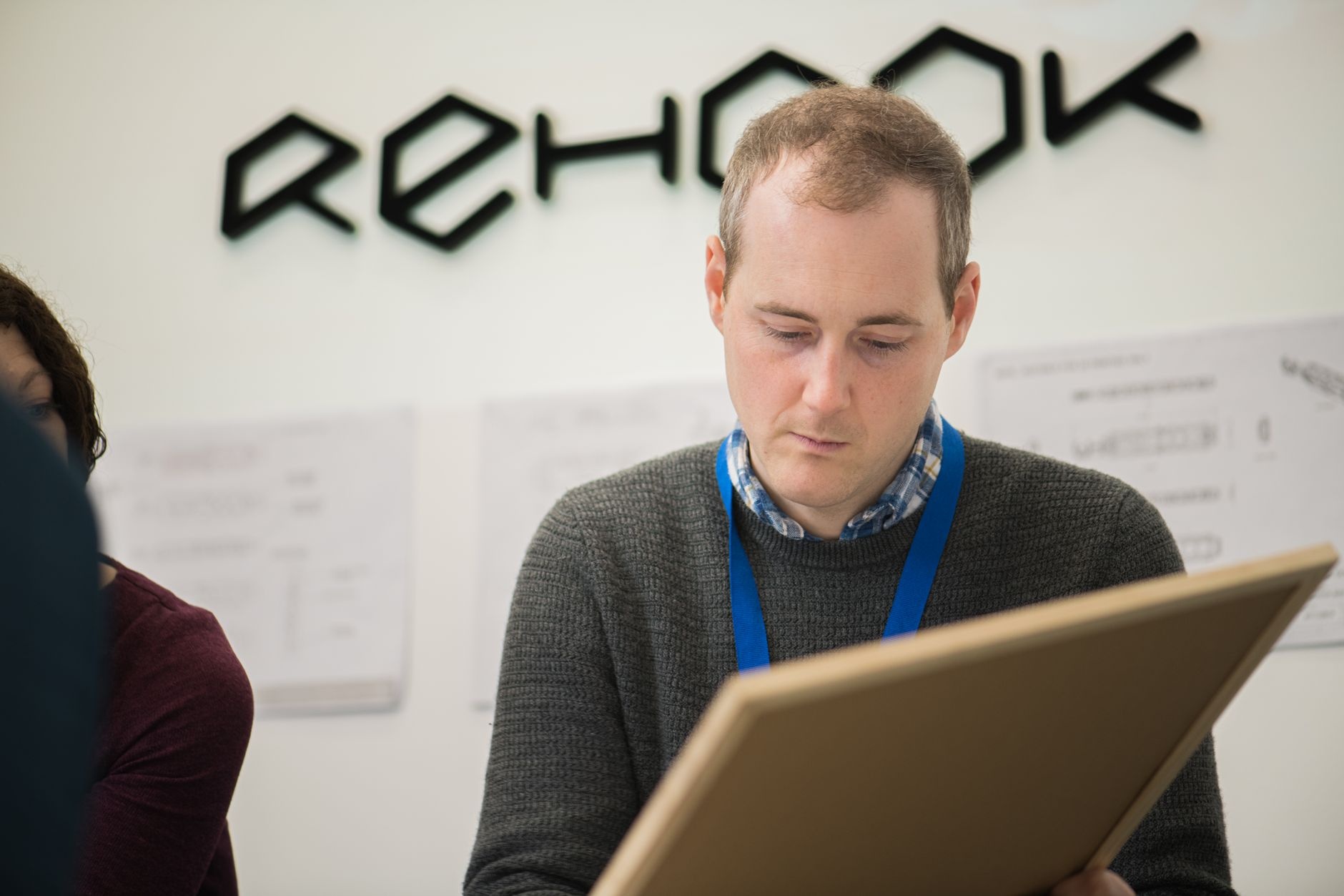 Adult man in a sweater, concentrating on a task or project in an office setting with visible charts.
