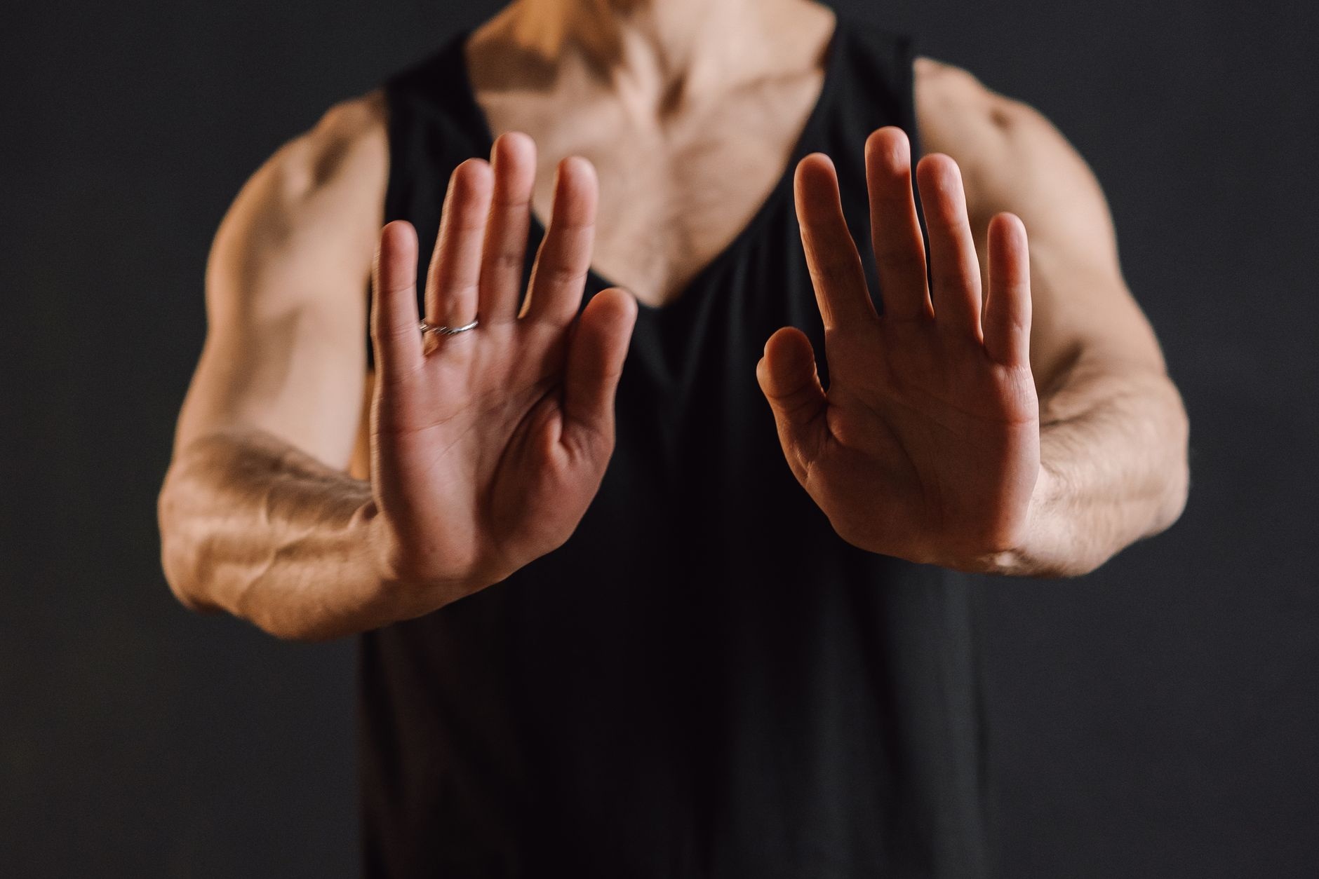 A focused close-up of a man in a black tank top performing a meditation gesture, hands in mudra.
