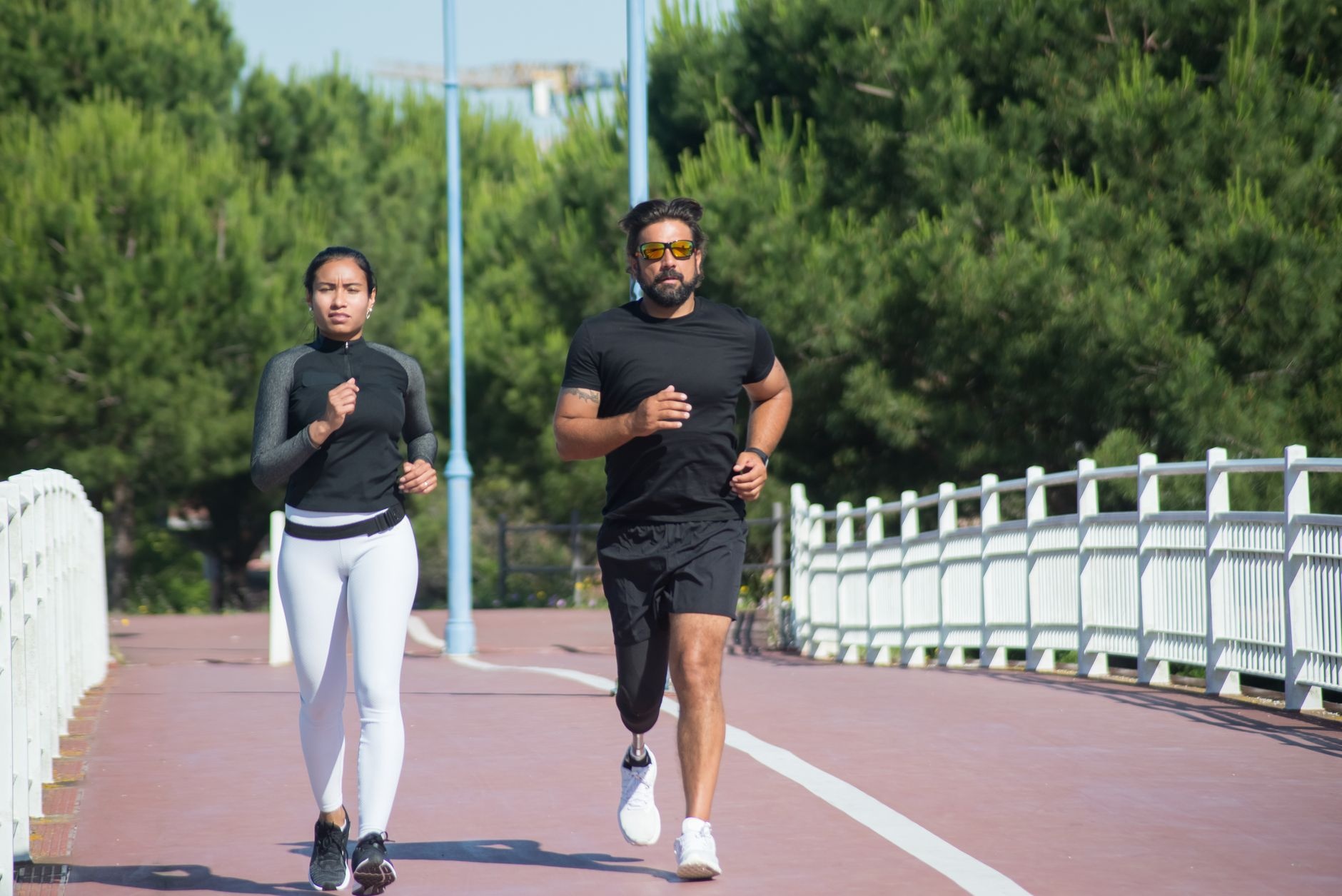 A couple jogging on a tree-lined path, enjoying an outdoor workout on a sunny day.