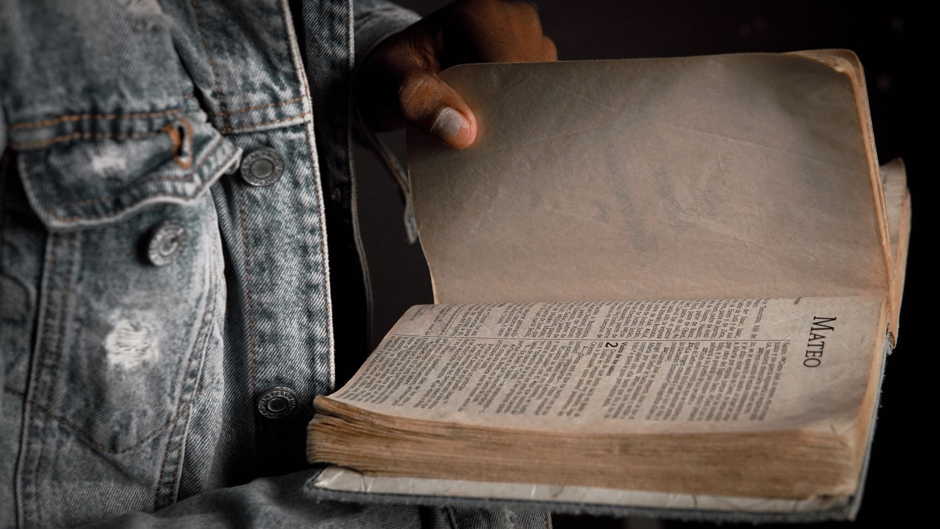 A person in a denim jacket holding an open Bible to the book of Matthew.
