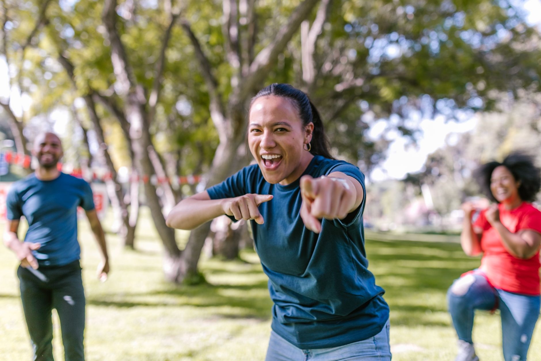 Three adults enjoying a team-building activity outdoors with vibrant smiles on a sunny day.