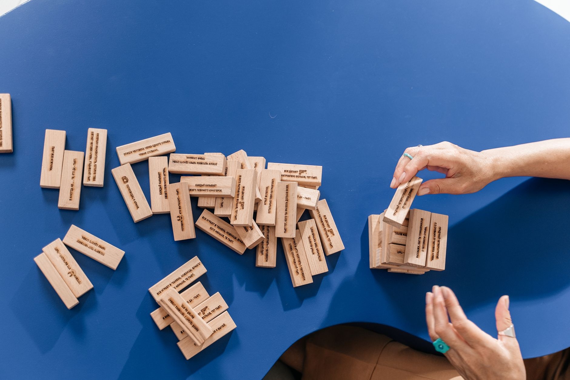 Close-up of hands stacking wooden Jenga blocks on a blue table, focusing on balance and strategy.