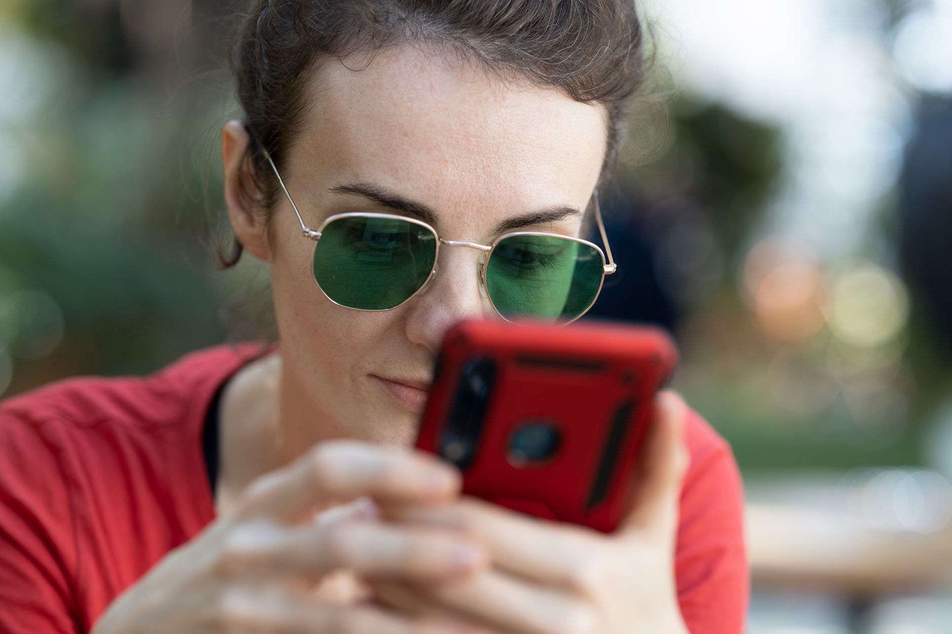 A woman in sunglasses attentively using a smartphone outdoors. Focus on technology and leisure.
